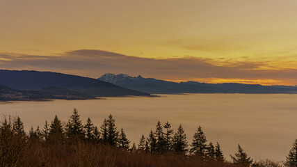 Golden sunrise over cloud-covered valley floor with mountains in silhouette on horizon.