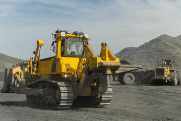 A bulldozer drives through an open quarry. The ore is being loaded in the background.