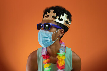 Black man in costume for carnival with pandemic mask isolated on orange background.