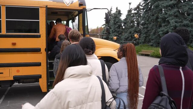 Rear view of multiracial high school students taking turns boarding yellow school bus after studies. Group of multi-ethnic secondary school pupils entering school bus one after another after class