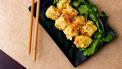 Chinese Steamed Dumpling served in a black plate on a wooden table. along with cilantro.