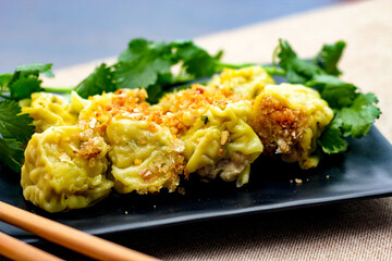 Chinese Steamed Dumpling served in a black plate on a wooden table. along with cilantro.