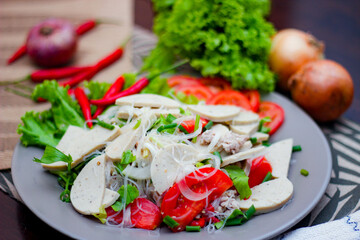 Spicy Glass Noodle Salad with Vietnamese Sausage  served in a gray plate Put on a wooden table and various vegetables.