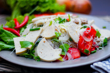 Spicy Glass Noodle Salad with Vietnamese Sausage  served in a gray plate Put on a wooden table and various vegetables.