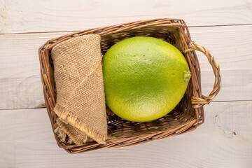 One juicy organic pomelo in a basket on a wooden table, macro shot, top view.

