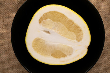 One half a juicy organic pomelo in a black ceramic dish on a burlap, macro view, top view.