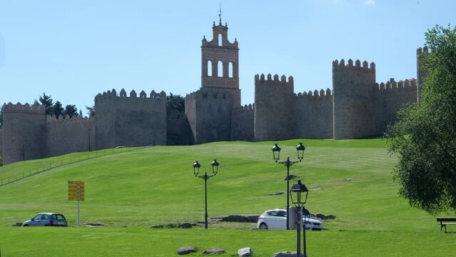 Busy road and exterior of fortified walls surround the medieval spanish city of Avila on background, sunny daytime view against blue clear sky. Landmark in Castile and Leon. UNESCO. Spain