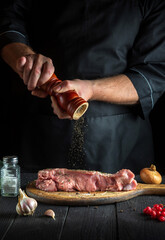 Professional chef prepares raw veal meat. Before baking, the chef adds pepper to beef. National dish is being prepared in the restaurant kitchen