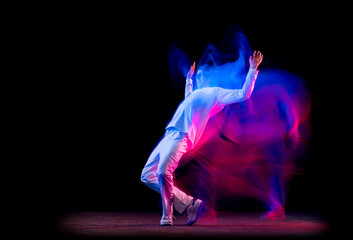 Dynamic portrait of male hip-hop dancer dancing isolated on dark background in mixed neon light. Youth culture, hip-hop, movement, style and fashion, action.