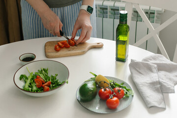 Woman preparing vegetable salad with tomato in the kitchen. Healthy food vegan salad. Mindful eating