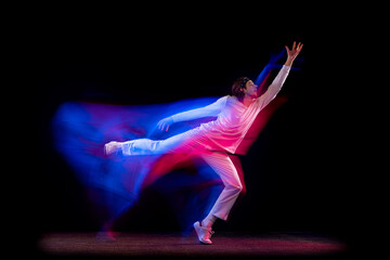 Dynamic portrait of male hip-hop dancer dancing isolated on dark background in mixed neon light. Youth culture, hip-hop, movement, style and fashion, action.
