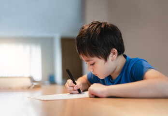 School kid using black pen drawing or writing the letter on paper, Young boy doing homework, Child with pen writing notes in paper sheet during the lesson.Cute pupil doing test, Homeschooling concept