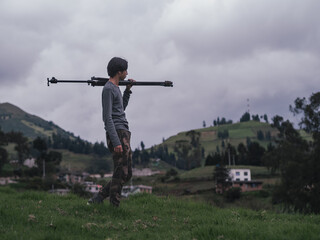 young latin man carrying a tripod up a hill in the highlands of Ecuador on a cloudy day