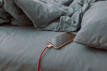 Mobile smart phone charging battery on bed in the bedroom at home. Technology, multiple sharing and lifestyle concepts