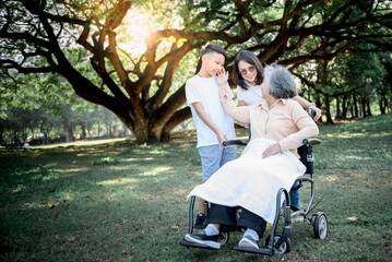 Asian elderly woman sitting in a wheelchair, smiling and happy with her daughter and grandson taking care of her, to relationship of Asian family and retirement age concept.
