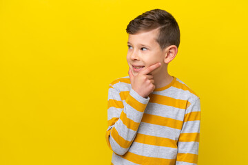 Little caucasian boy isolated on yellow background looking to the side and smiling