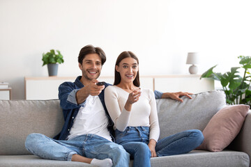 Happy laughing relaxed millennial european woman and man with remote control hugging, watching tv