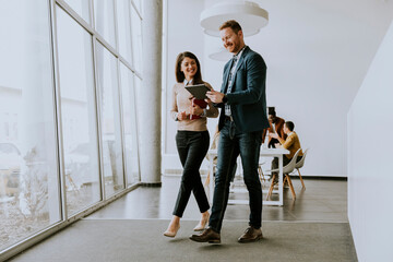 Young entrepreneur couple walking together and using digital tablet in the modern office
