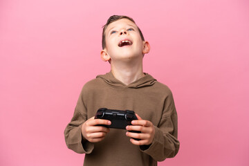 Little caucasian boy playing with a video game controller isolated on pink background laughing © luismolinero