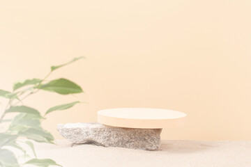 Round beige platform podium on grungy concrete stone on white beach sand with green plant leaves in foreground. Creative composition background for cosmetics or products presentation. Front view