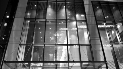 Amazing night cityscape. Office building at night, building facade with glass and lights. View with illuminated modern skyscraper. Scenic glowing windows of skyscrapers at evening. Black and white.