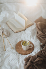 Cozy composition with a book, tea cup and knitting needles on bed sheets. Sweet home. 