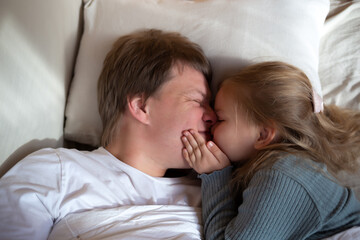 little cute girl hugging her dad while lying in bed