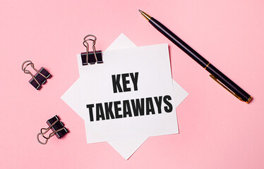 On a light pink background, black paper clips, black pen and white note paper with the words KEY...
