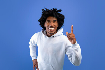 Cool black teenager having creative idea, pointing upwards, experiencing AHA moment on blue studio background