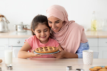 Happy Muslim Mother And Cute Little Daughter Holding Homemade Pie In Kitchen