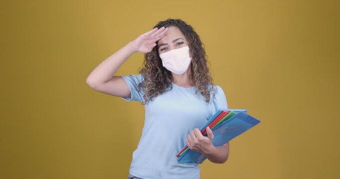 Afro brazilian, latin american woman, university student, wearing face mask against virus, protection, security, waving hand to forehead, smiling and looking at camera. holding notebooks and books, ye
