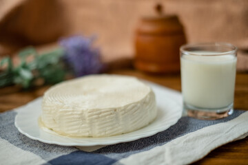 Fototapeta na wymiar A glass of goat milk and a head of goat milk cheese stand on a wooden table. Cheese at home.