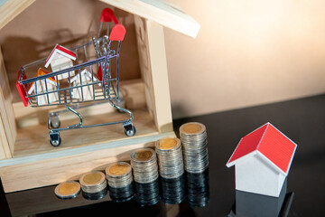 Buying property or real estate investment concept. Home mortgage and lease. Bank loan interest rate. Wooden house models in mini shopping cart with step of coins stacked on glossy table.