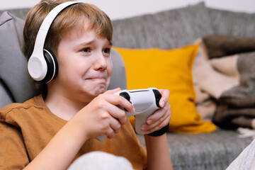 Sad teen boy upset by losing video game. A gamer with joystick in his hands plays the console © LunaLu