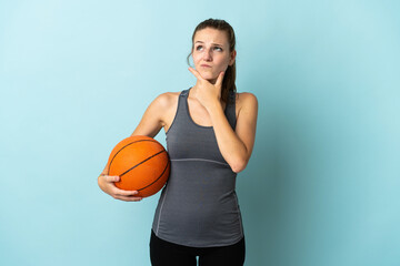 Young woman playing basketball isolated on blue background having doubts