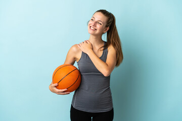 Young woman playing basketball isolated on blue background looking up while smiling