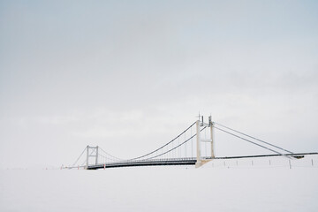 Fototapeta premium Suspension bridge over snow under cloudy sky in winter