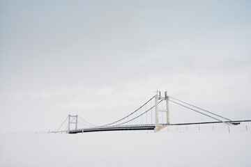 Suspension bridge over snow under cloudy sky in winter