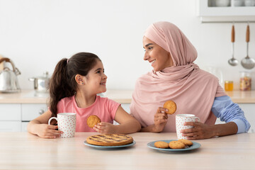 Obraz na płótnie Canvas Portrait Of Happy Islamic Family Mom And Daughter Eating Snacks In Kitchen