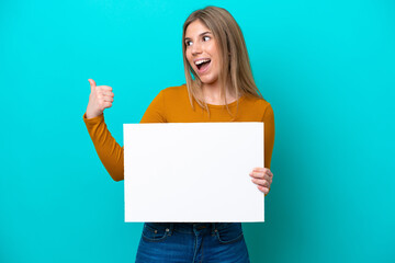 Young caucasian woman isolated on blue background holding an empty placard and pointing side