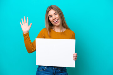 Fototapeta premium Young caucasian woman isolated on blue background holding an empty placard and saluting