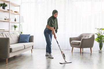 Muslim woman cleaning floor with spray mop in living eoom