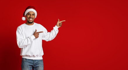 Positive black man in Santa hat pointing at copy space