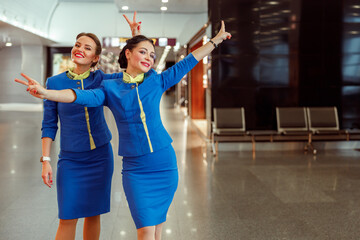 Joyful female flight attendants in air hostess uniform doing peace hand gesture and smiling while...