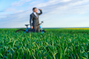 business concept - A businessman rides a bicycle on a green grass field, looks into the distance,...
