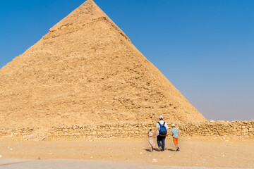 Father and children walk in front of the Chephren pyramid on the Giza plateau. - obrazy, fototapety, plakaty