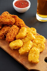 Homemade Crispy Fried Chicken Wings and Nuggets on a rustic wooden board on a black surface, side view.