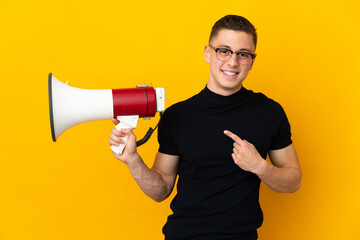 Young caucasian man isolated on yellow background holding a megaphone and pointing side