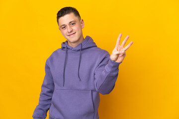 Young caucasian man isolated on yellow background happy and counting three with fingers