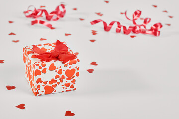 A small white box with red hearts on a white background, paper hearts scattered nearby